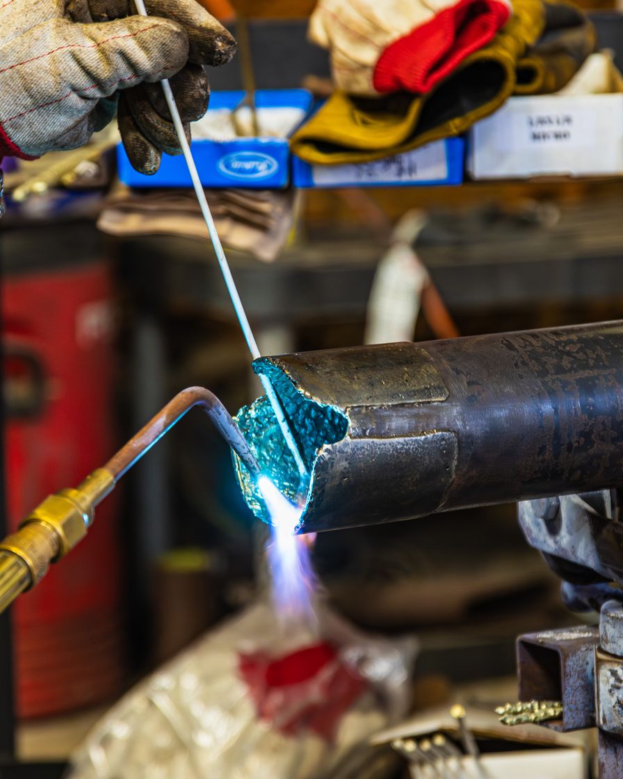 A Python Downhole Tools technician brazing a downhole tool joint in the Corpus Christi shop, torch flame on the workpiece.