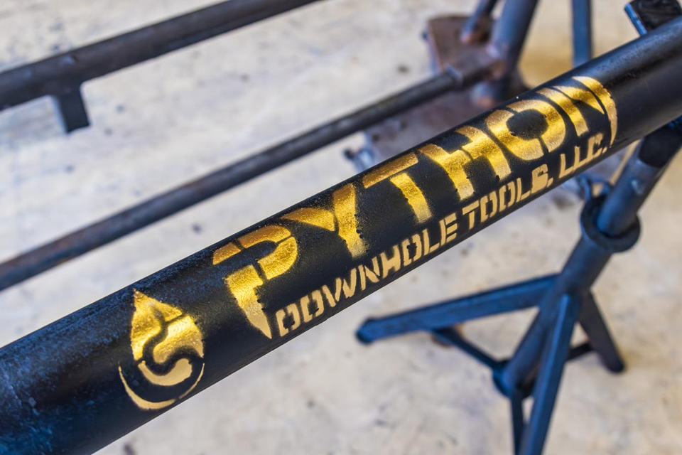 Close-up of a downhole tool body stencilled in gold with the Python Downhole Tools, LLC mark.